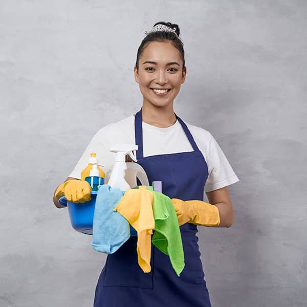 A house cleaner smiling while holding cleaning supplies