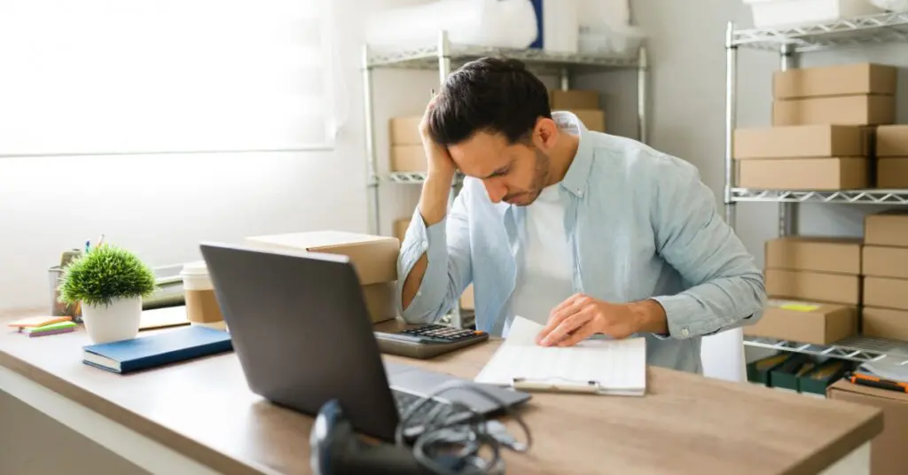 Small business owner at a cluttered desk looking stressed while checking marketing analytics on a laptop