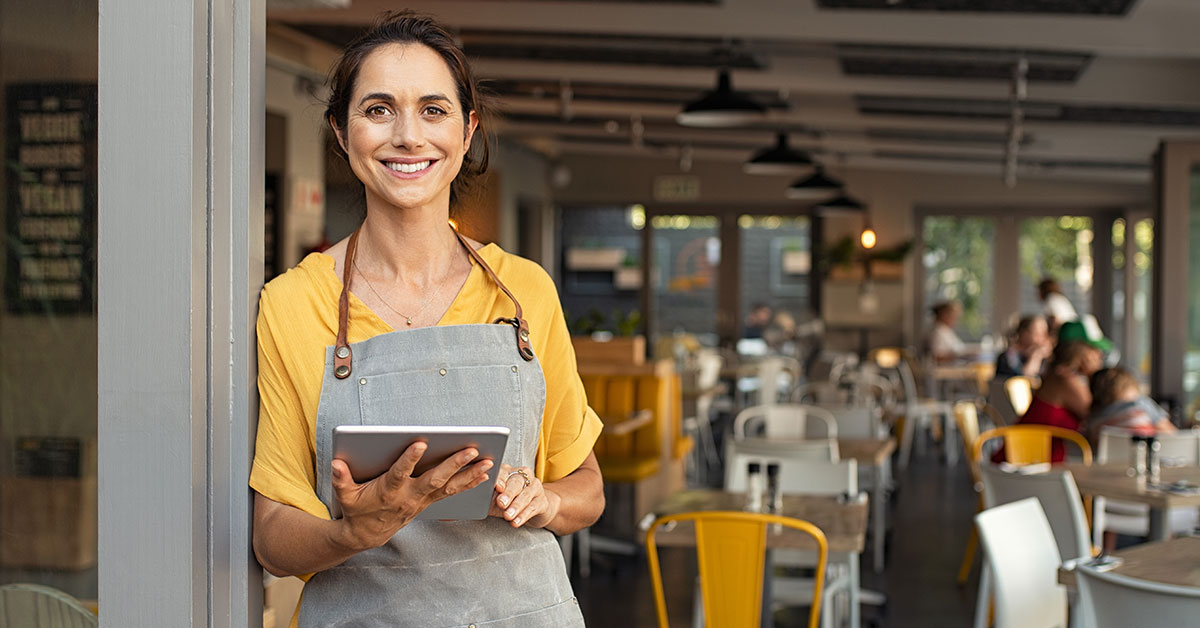 Confident small business owner standing in front of their shop with an open sign, smiling and optimistic