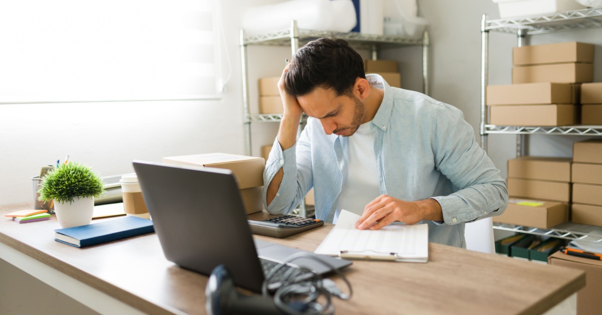 Small business owner at a cluttered desk looking stressed while checking marketing analytics on a laptop